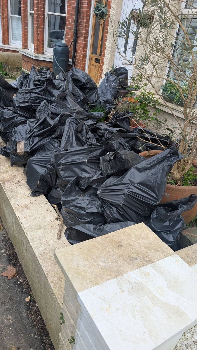 Front garden of a terraced house piled with black rubbish bags