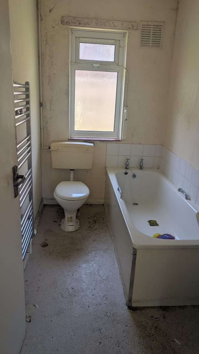 The same bathroom with the towels, mat and bottles gone, leaving the fitted bath, toilet and a marked floor