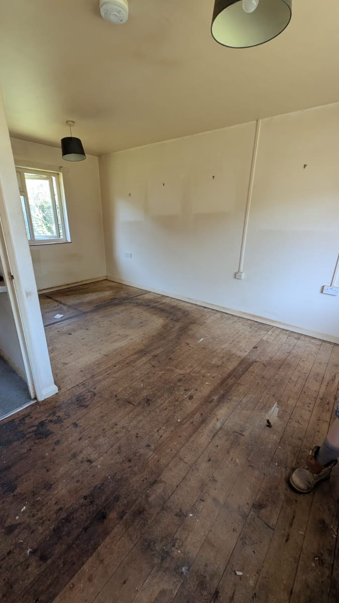An empty room with bare wooden floorboards and plain walls after clearance